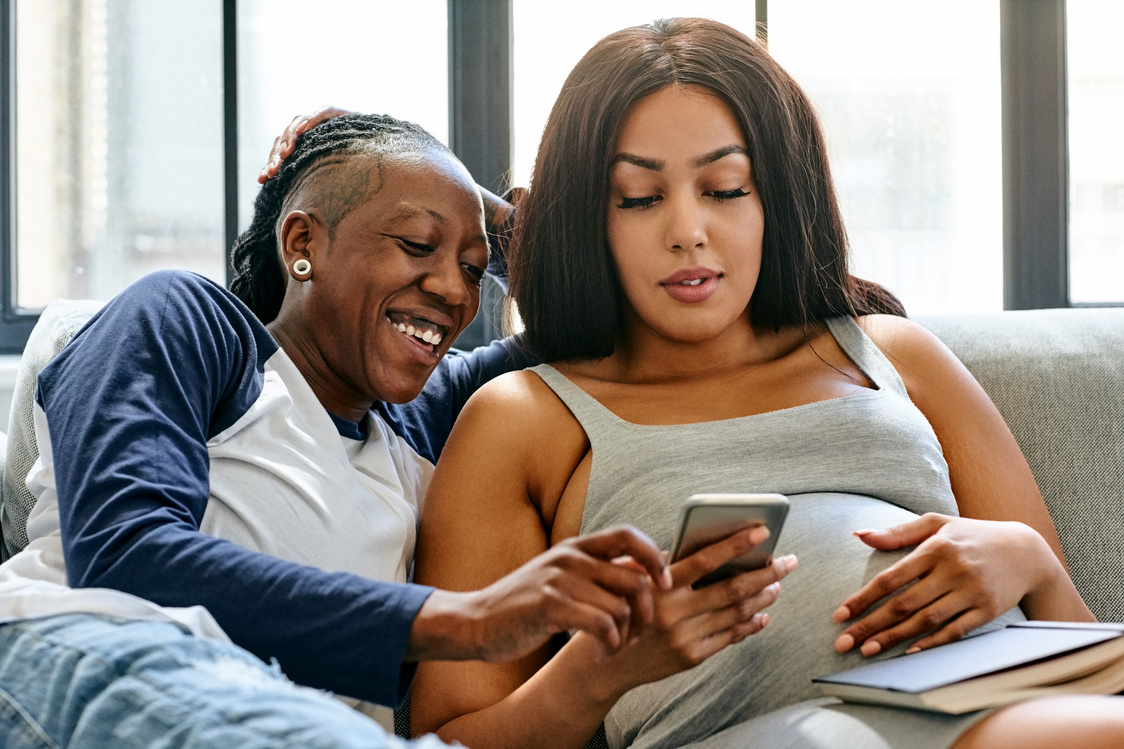 Pregnant lesbian couple relaxing on sofa with mobile phone